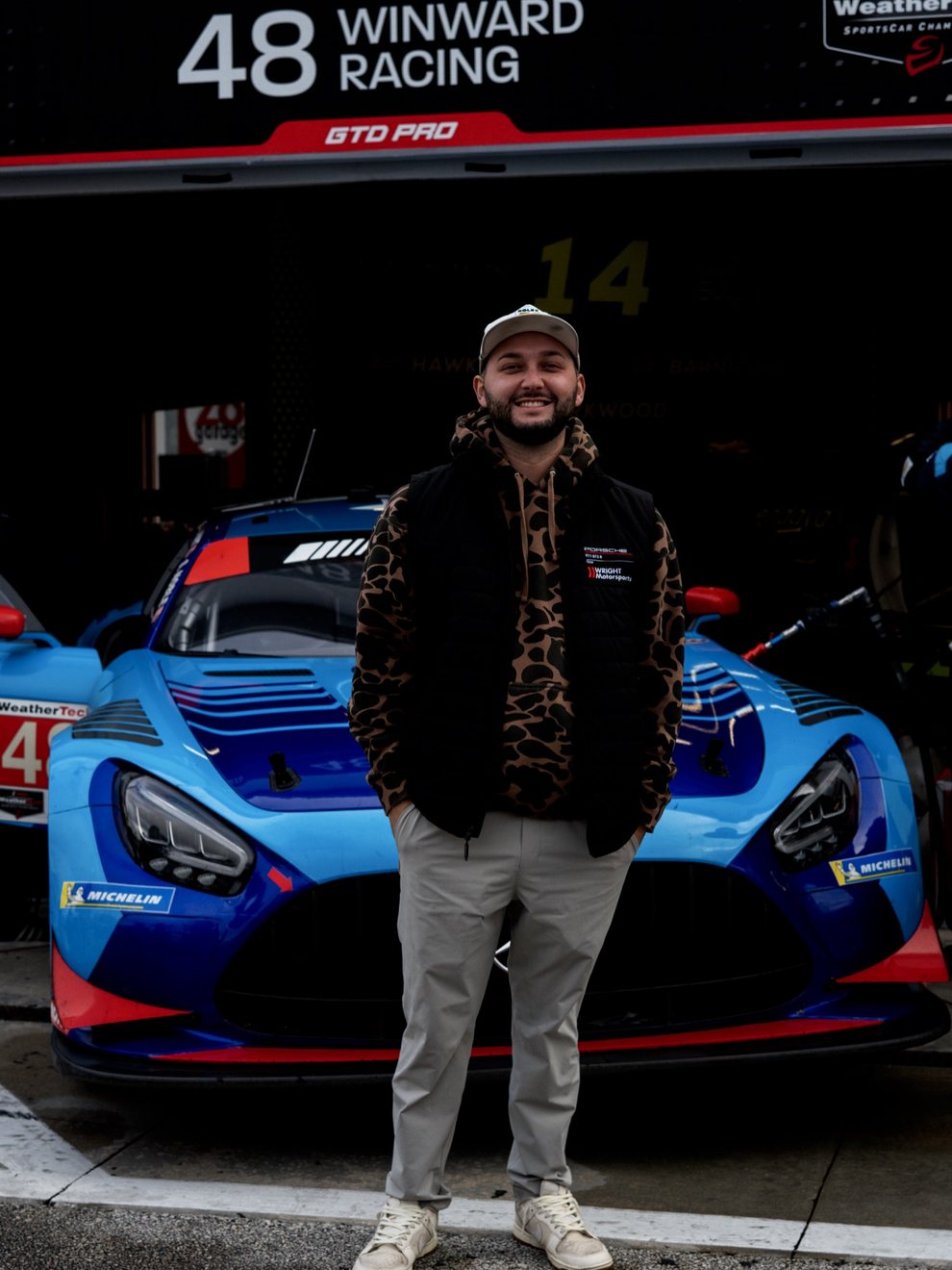 Wyatt Peavy, founder of Faceless Marketing, standing in front of the Winward Racing IMSA GTD Pro car in the paddock